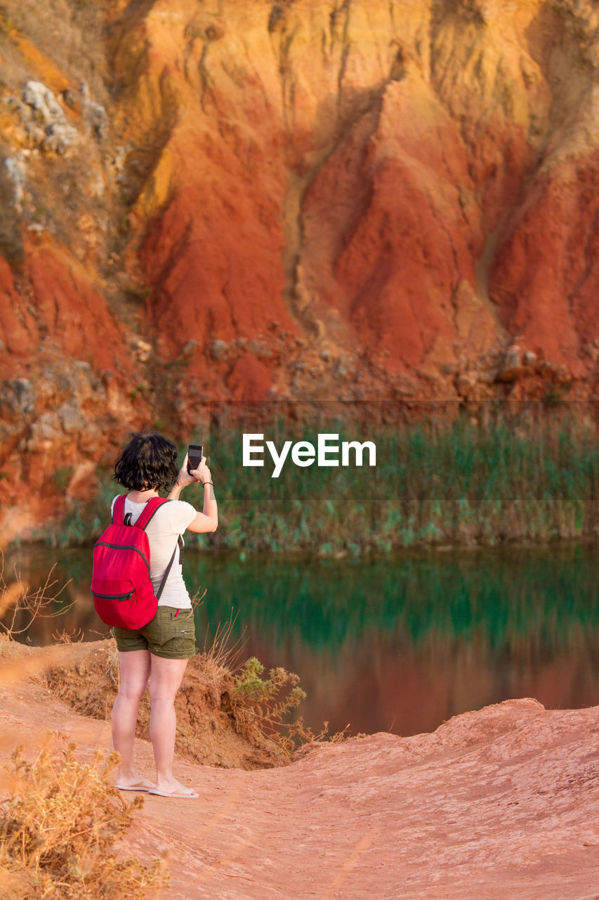 REAR VIEW OF WOMAN STANDING ON ROCK AT LAKE