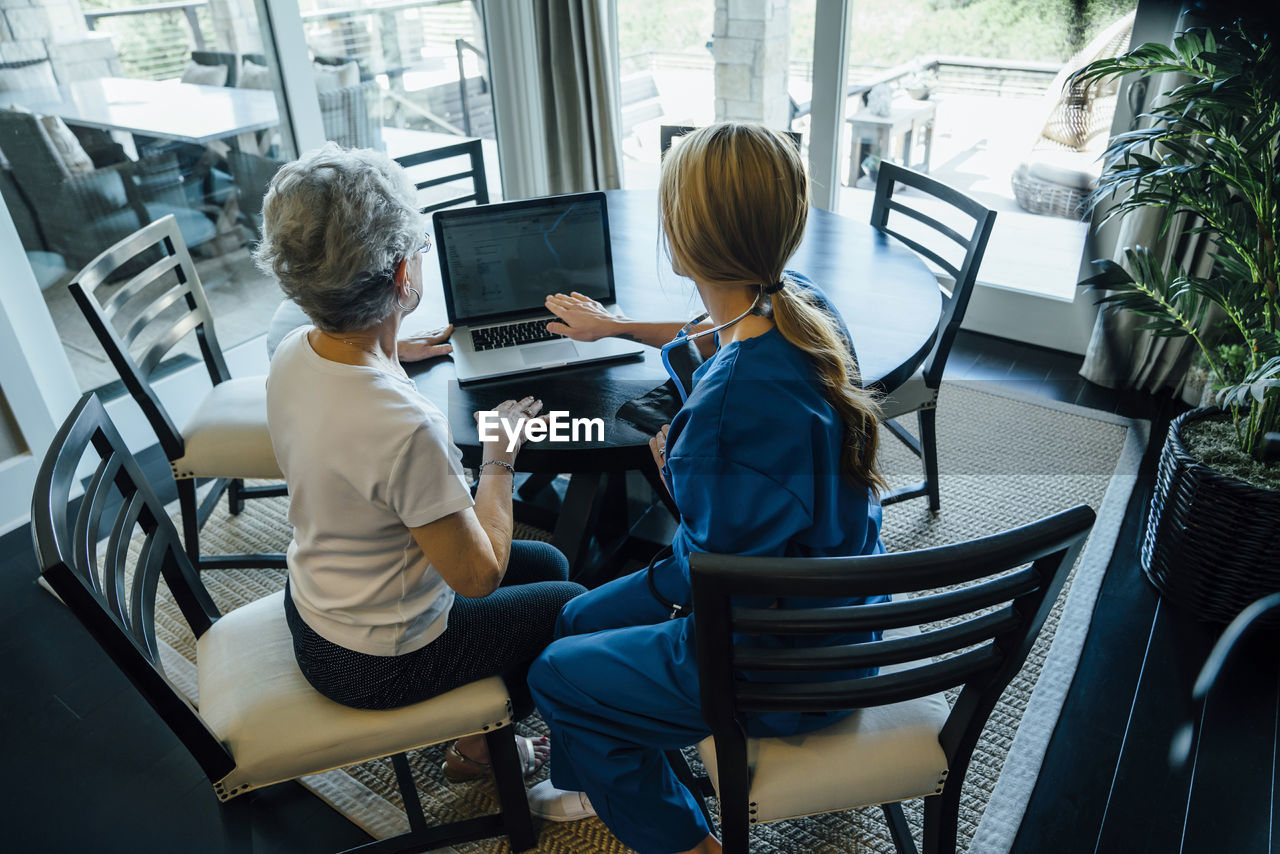 High angle view of home caregiver discussing over laptop computer with senior woman at dining table