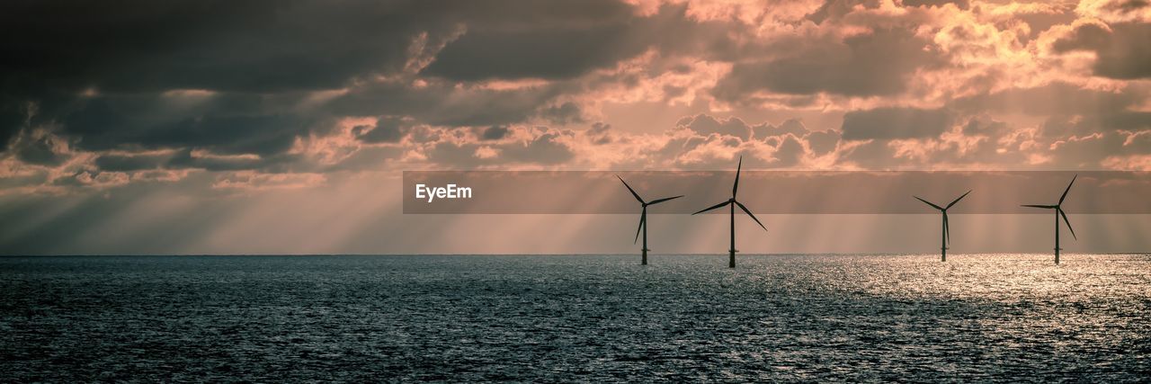 Windmills in sea against sky during sunset