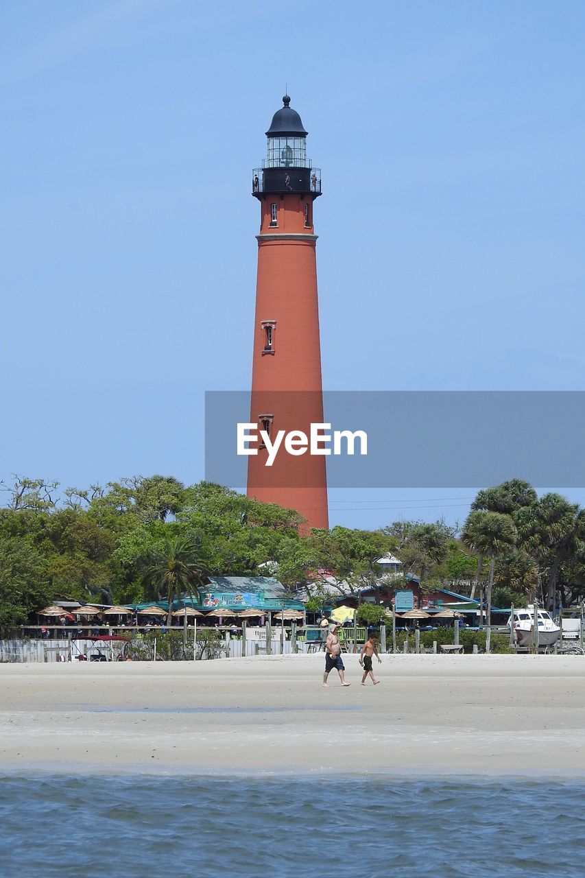 LIGHTHOUSE ON BEACH BY SEA AGAINST CLEAR SKY