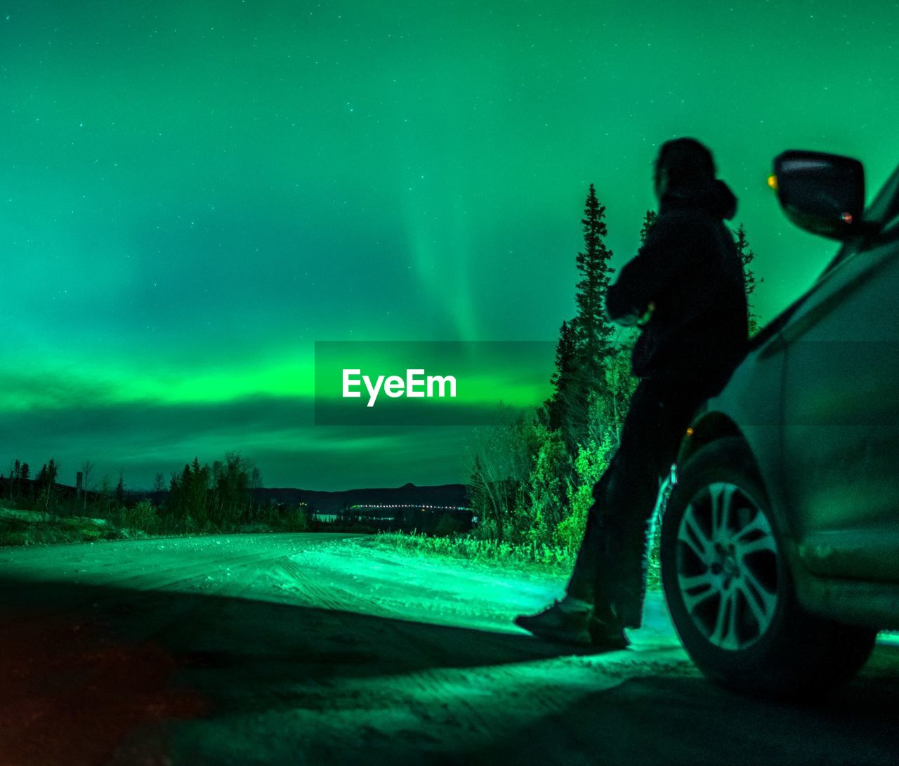 Person leaning on car against aurora polaris at night