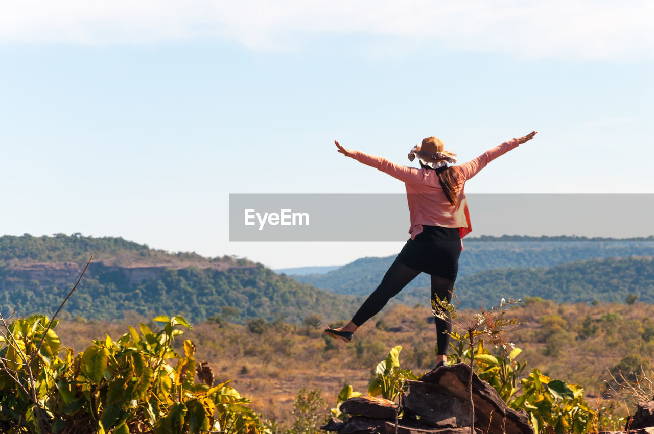 Full length of woman with arms outstretched against sky