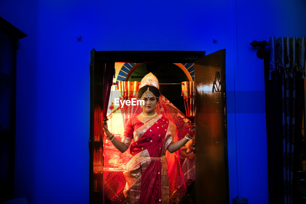 PORTRAIT OF WOMAN STANDING BY ILLUMINATED WALL AT NIGHT