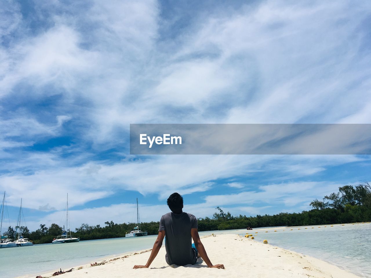 Rear view of man sitting at beach against sky