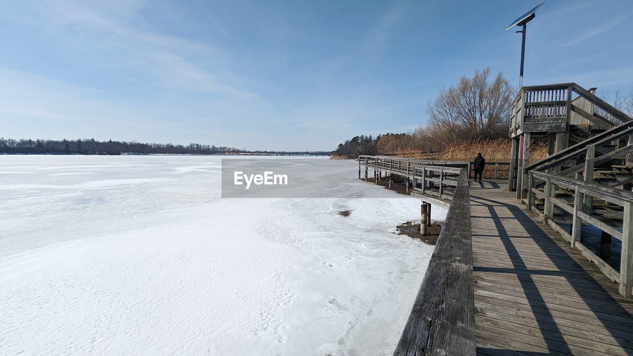 winter, snow, sky, water, cold temperature, nature, architecture, scenics - nature, environment, built structure, beauty in nature, landscape, day, ice, frozen, no people, land, cloud, wood, shore, sea, tranquility, outdoors, tranquil scene, walkway, blue, freezing, travel destinations, non-urban scene, tree, boardwalk, travel, pier, beach