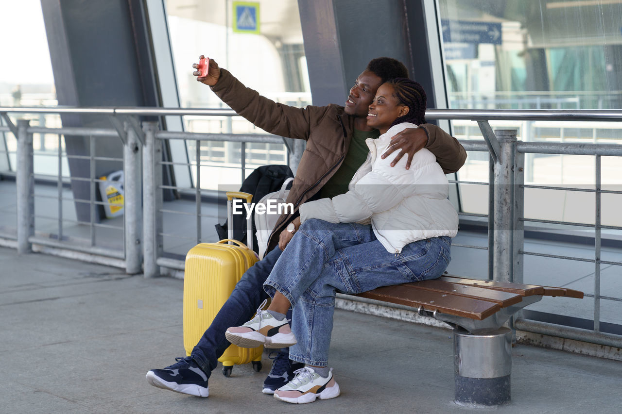 Happy couple of tourists take selfie at airport after arrival, loving african man and woman travel