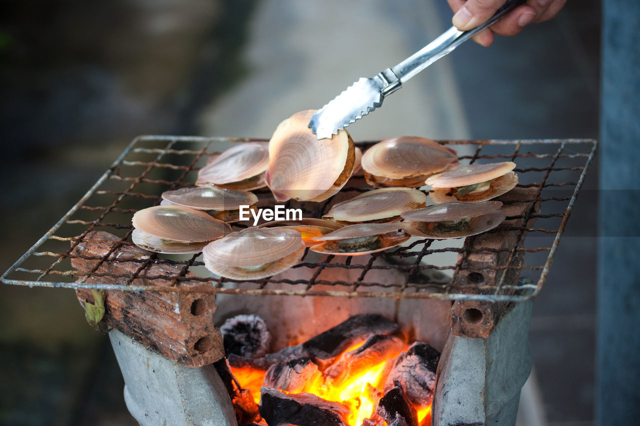 Cropped hand with mussels on barbecue grill