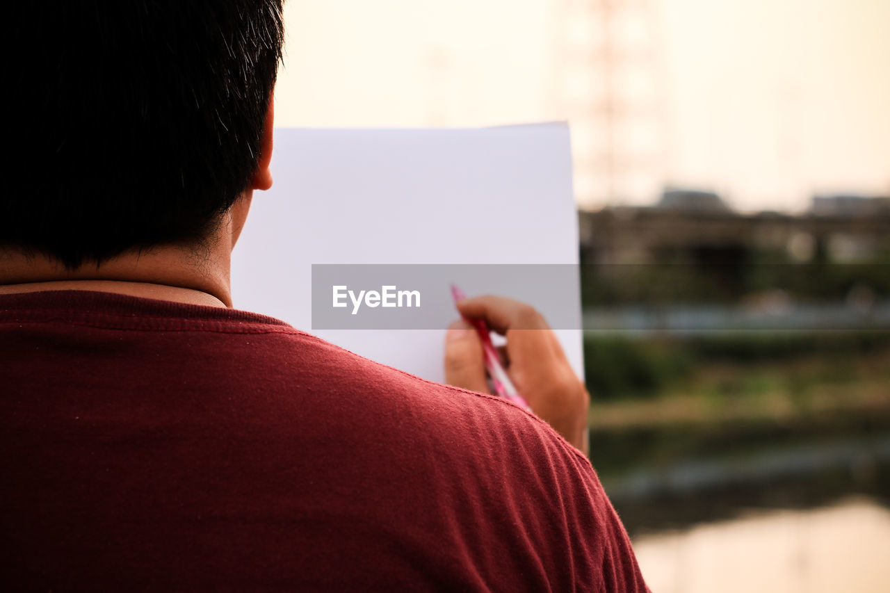 Rear view of man with blank paper in city during sunset