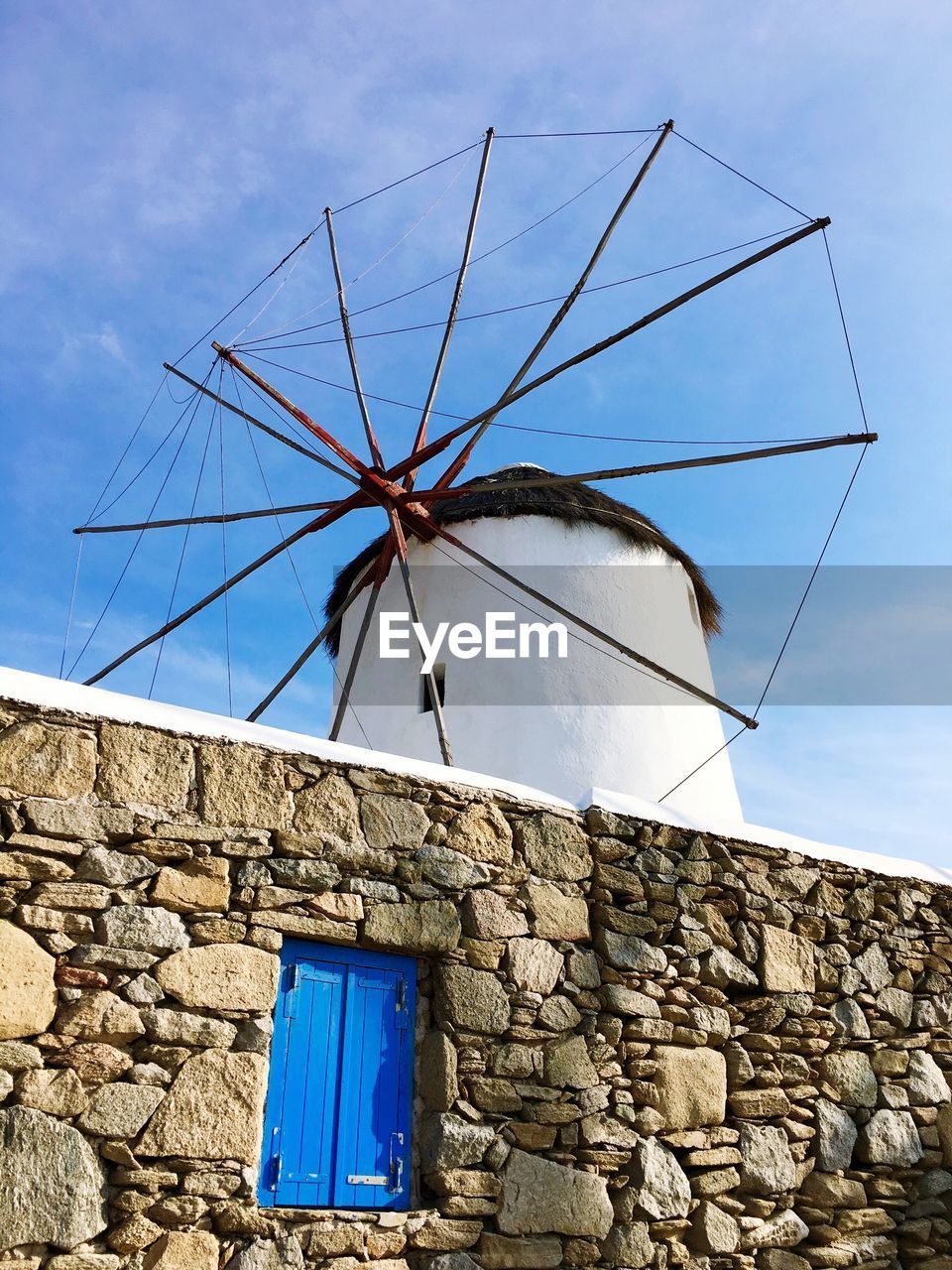 Low angle view of traditional windmill by wall against sky
