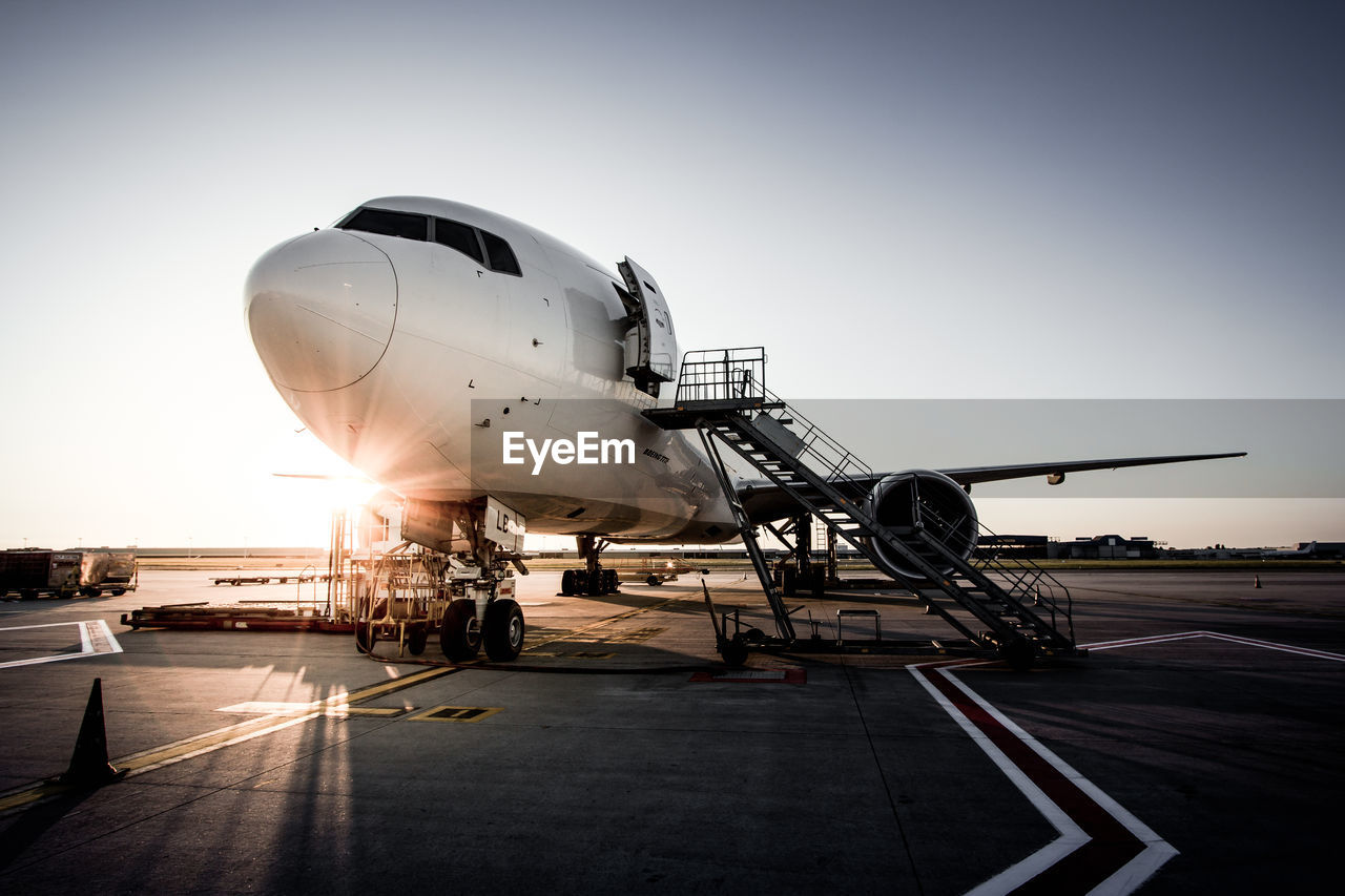 Airplane by ladder on runway against clear sky