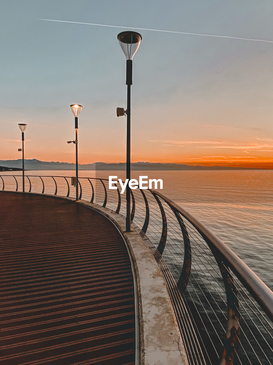 A pier with street lights at the sunset. sea and mountains view