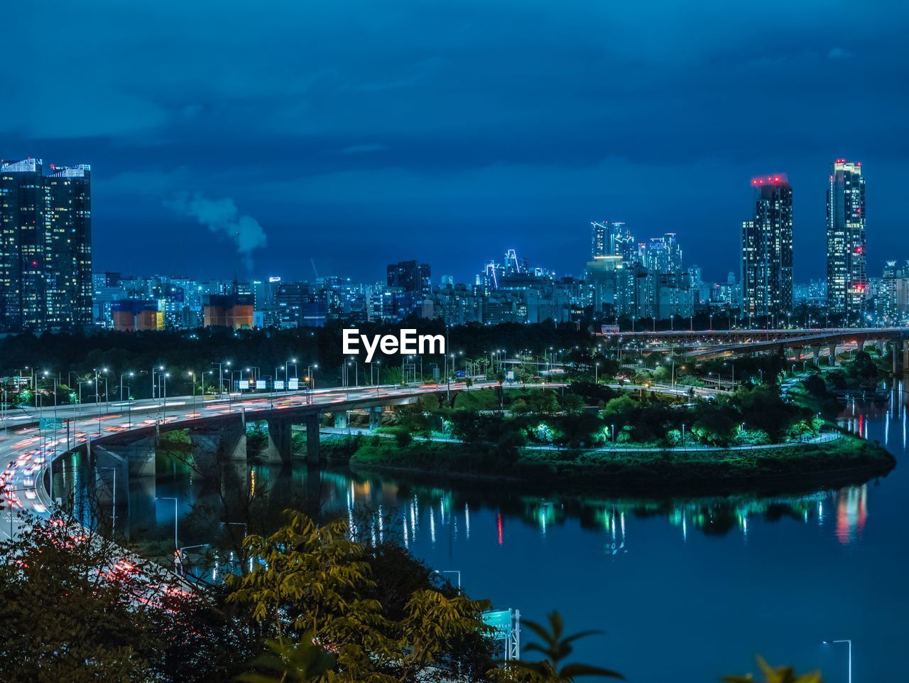 Illuminated buildings by river against sky at night