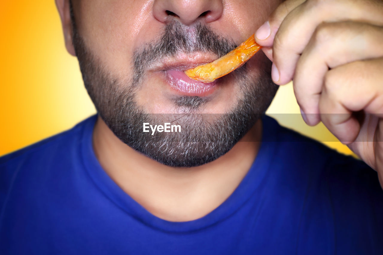 Close-up of a hungry man biting into a prawn. irresistible craving for food. yellow background.