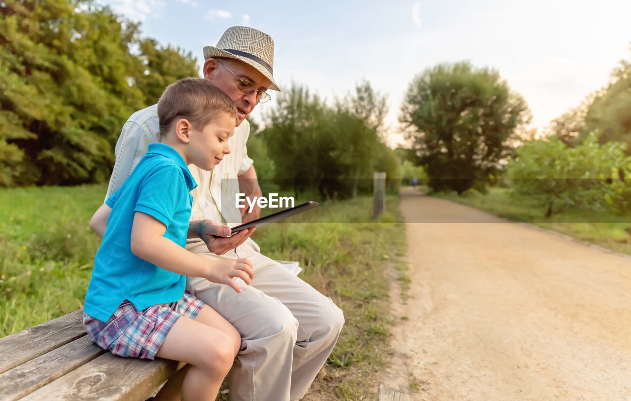 Grandson teaching digital tablet to grandfather while sitting in public park