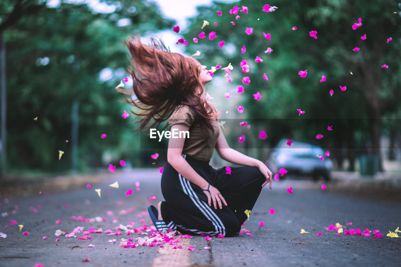 Side view of young woman with petals kneeling on street