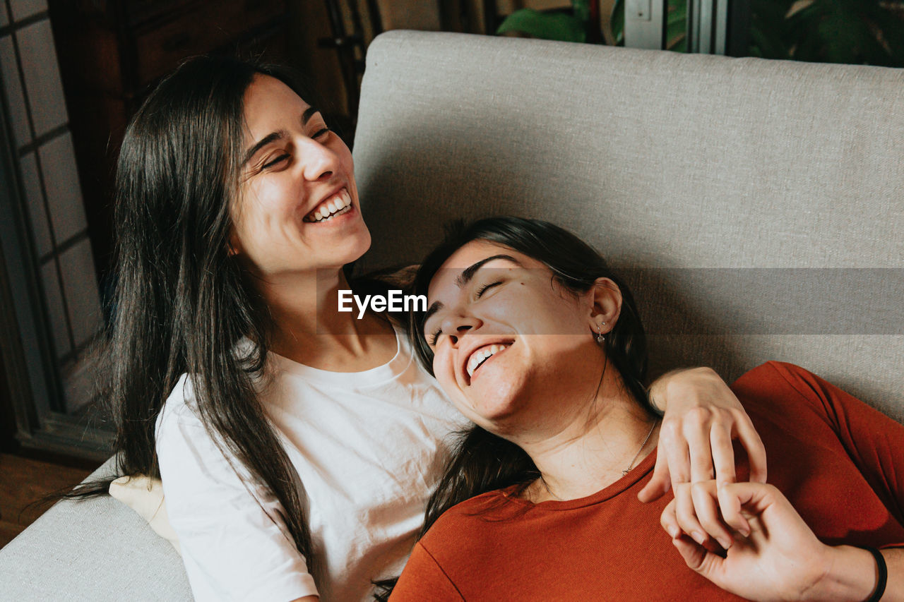 Lesbian couple embracing while lying on sofa at home