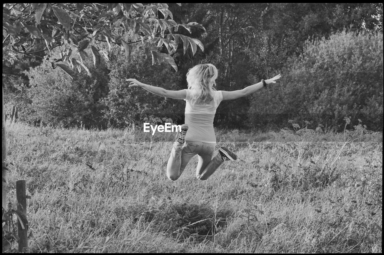 Rear view of woman jumping over plants against trees