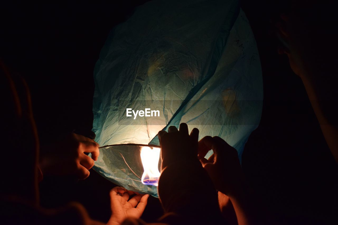 Cropped hands of friends holding lit paper lantern at night