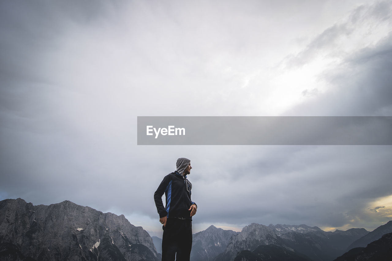 MAN STANDING ON MOUNTAIN AGAINST SKY DURING WINTER