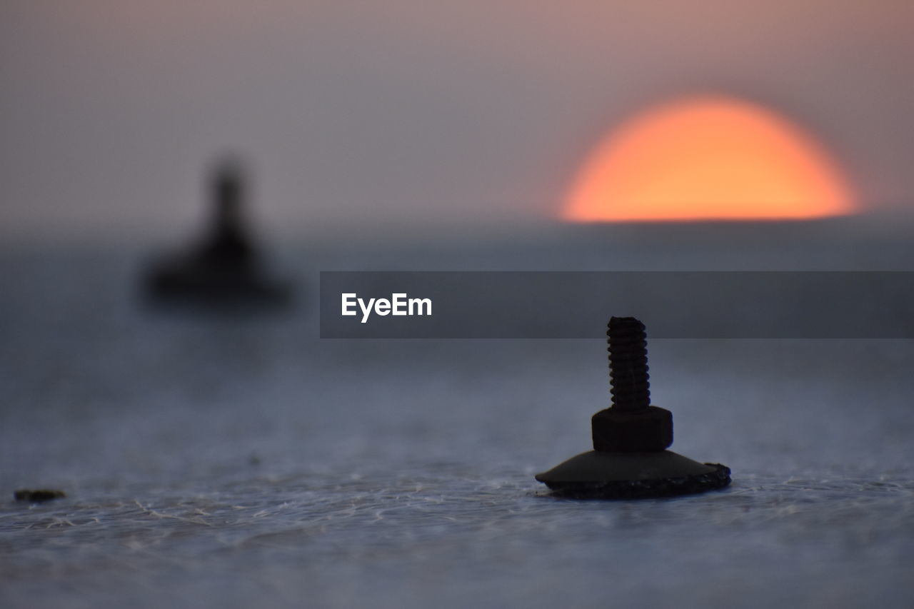 Close-up of rock in sea against sky during sunset