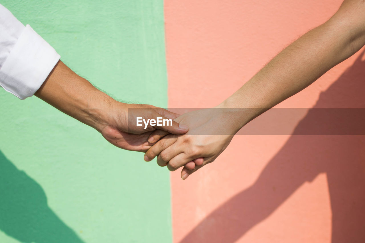 Cropped image of people with holding hands against wall