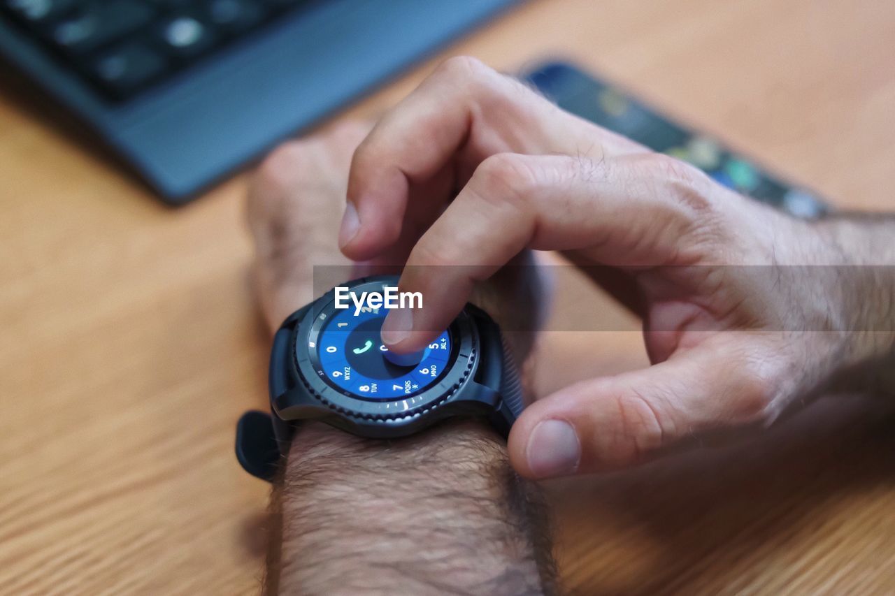 Cropped hand of man touching smart watch