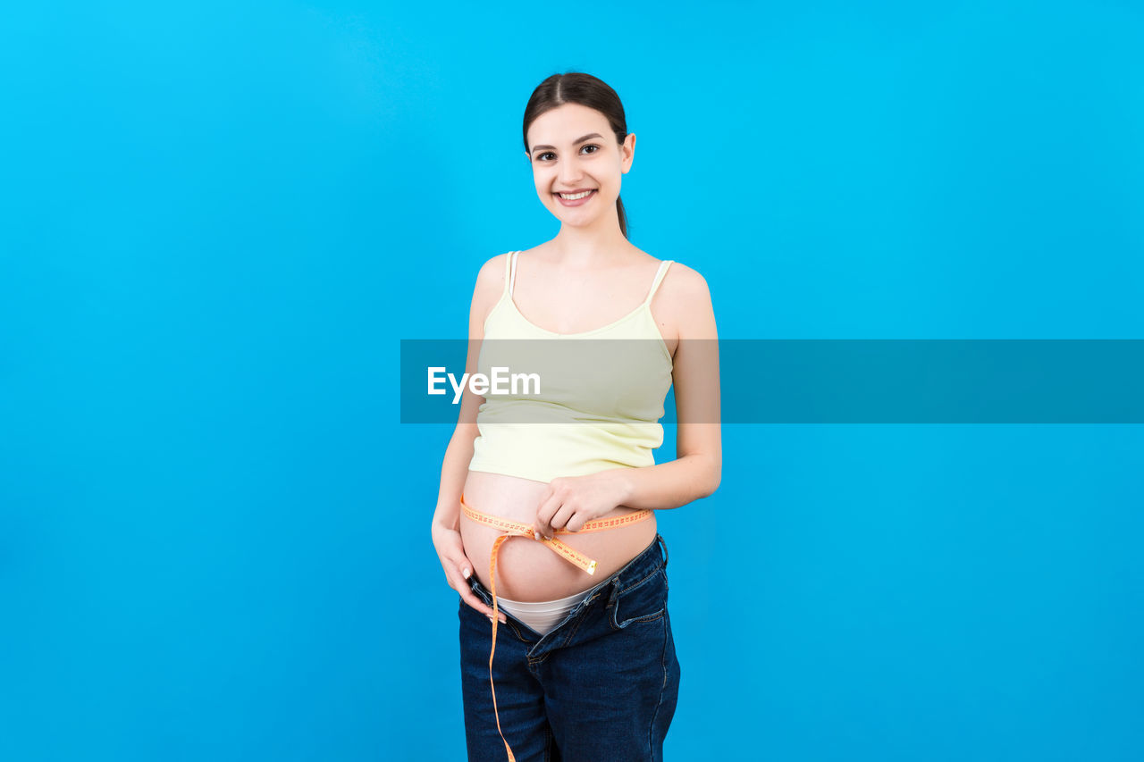 PORTRAIT OF A SMILING YOUNG WOMAN OVER BLUE BACKGROUND