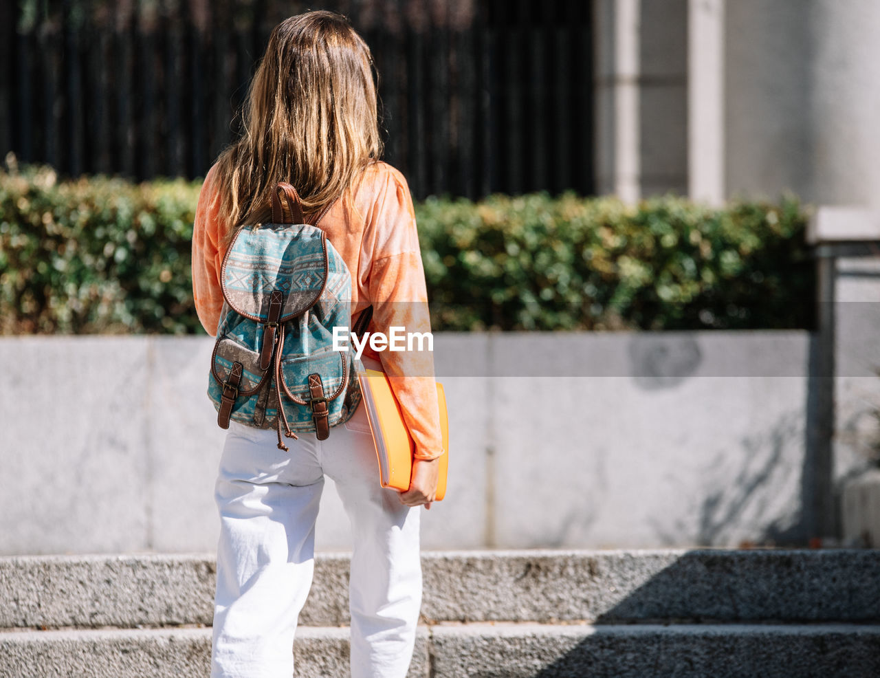 Back view of anonymous young female with backpack and notepad walking to studies on sunny day on street of madrid, spain