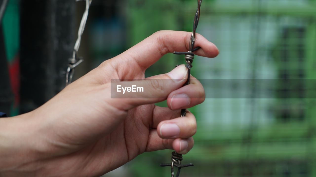 Close-up of hand holding barbed wire