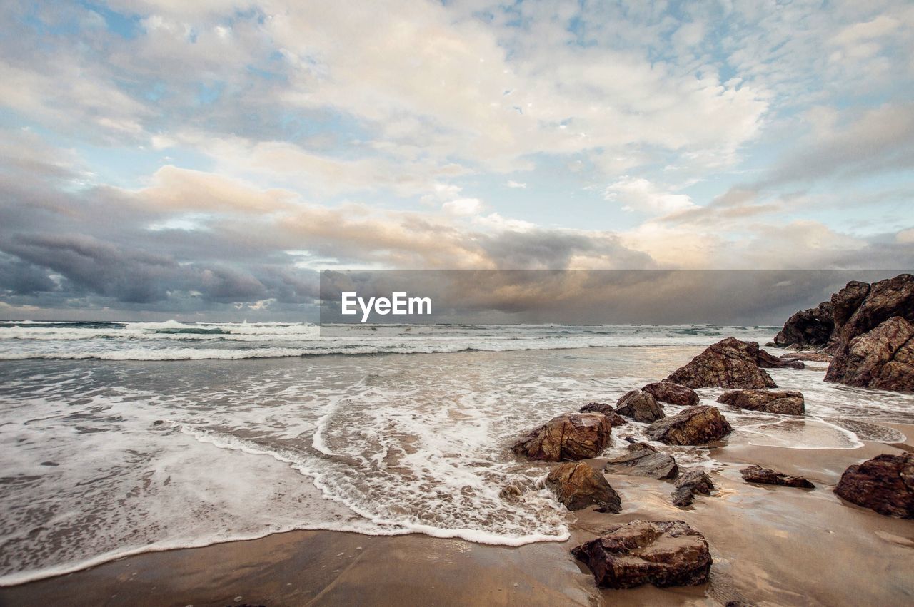 SCENIC VIEW OF ROCKY BEACH AGAINST SKY