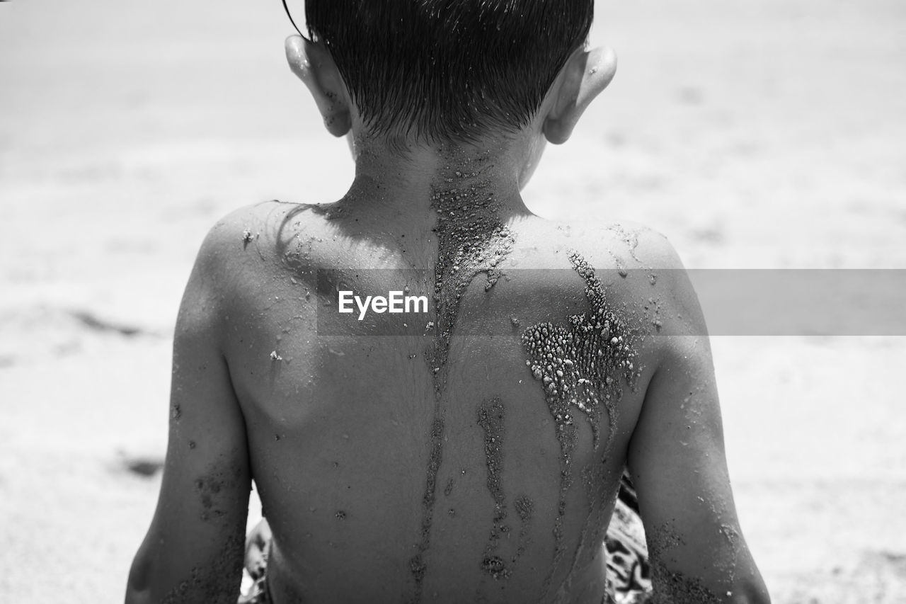 CLOSE-UP OF SHIRTLESS BOY STANDING ON BEACH