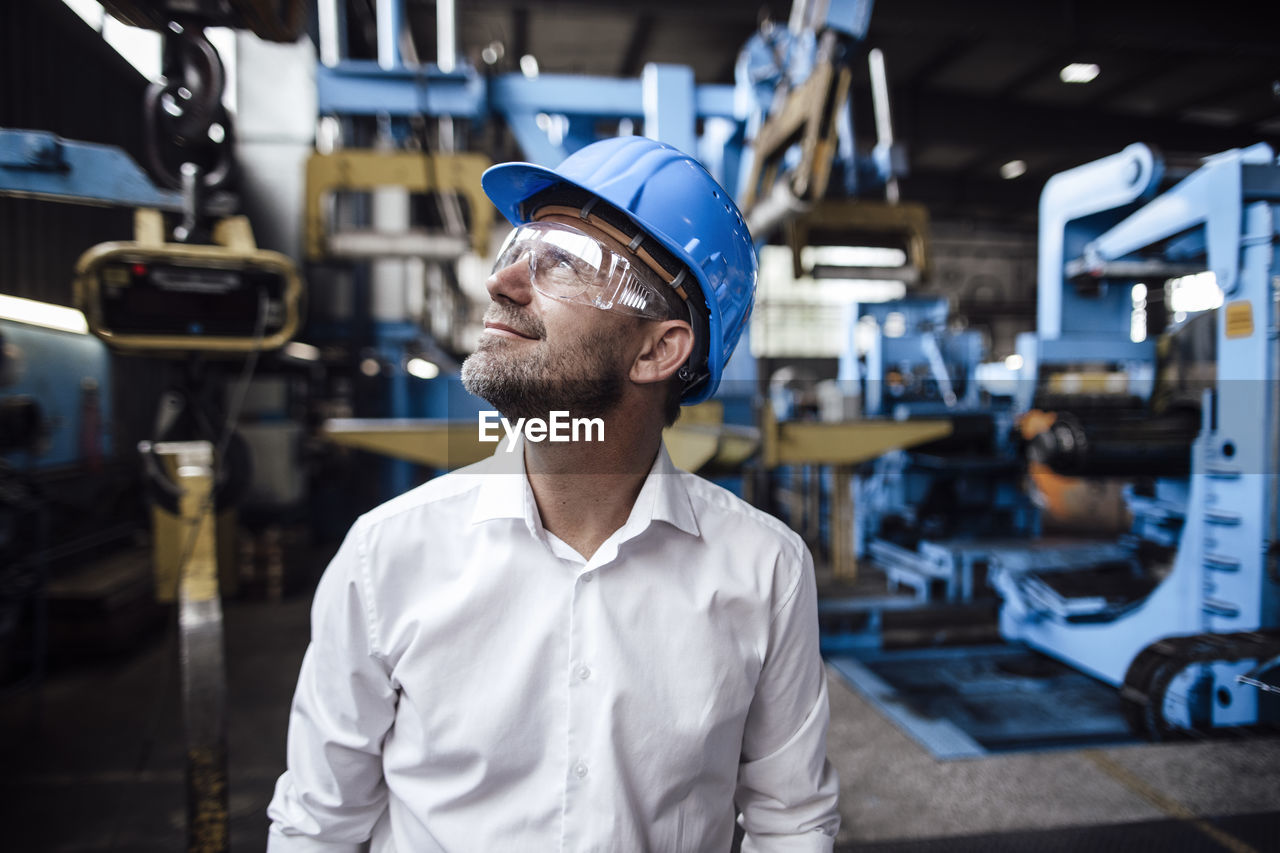 Smiling male entrepreneur looking up while wearing protective eyewear at factory