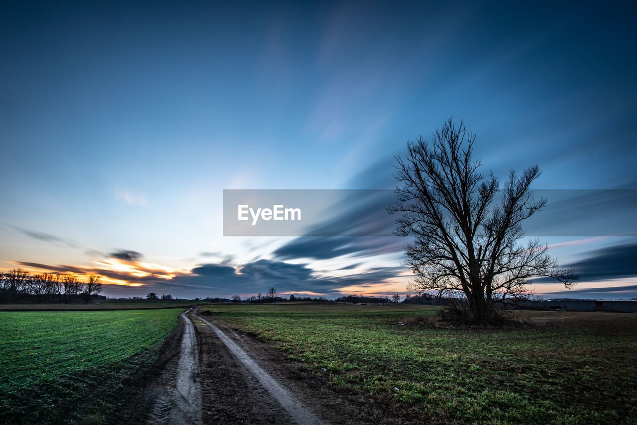 Empty road amidst field against sky at sunset