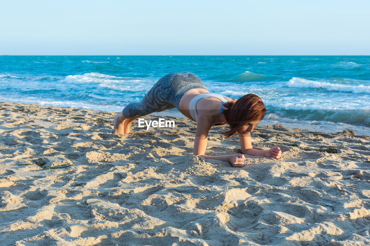 Woman exercising at sandy beach against sky