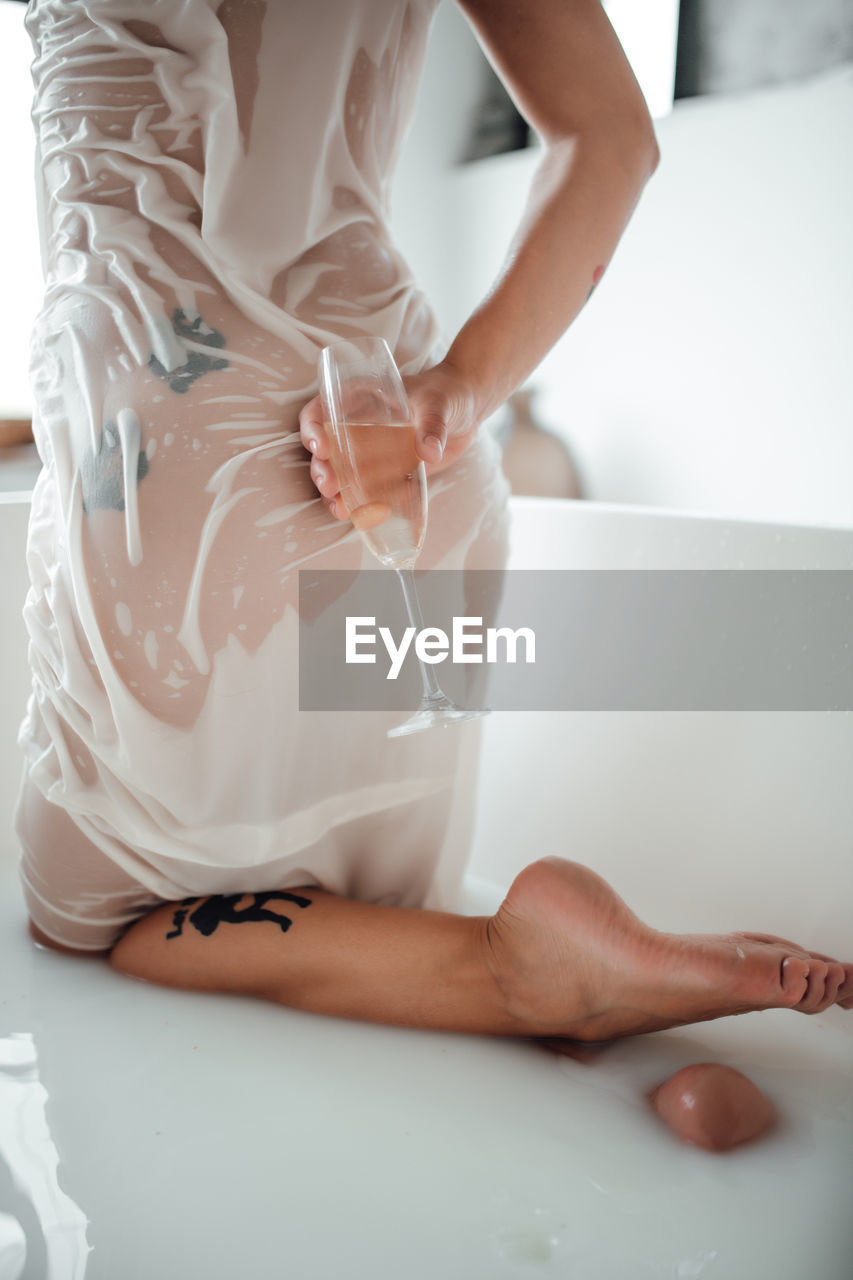 Midsection of woman holding drink in bathtub