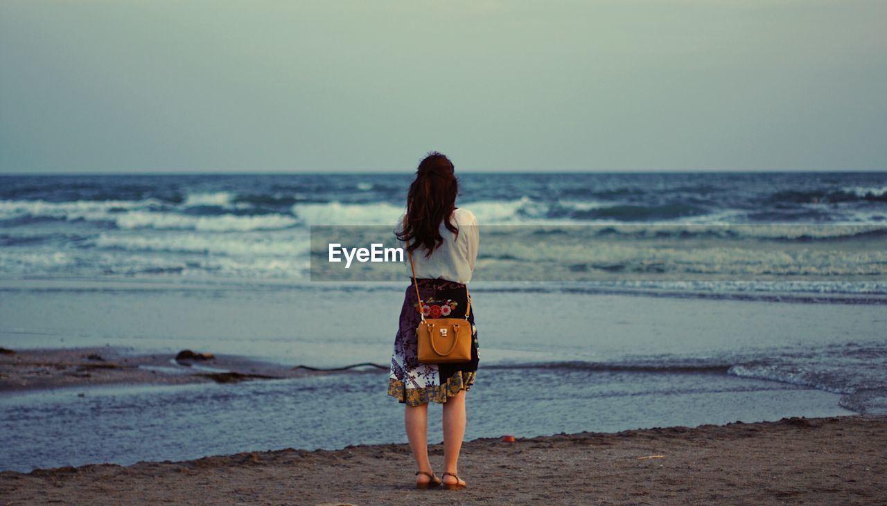 Rear view of woman standing at beach against sky