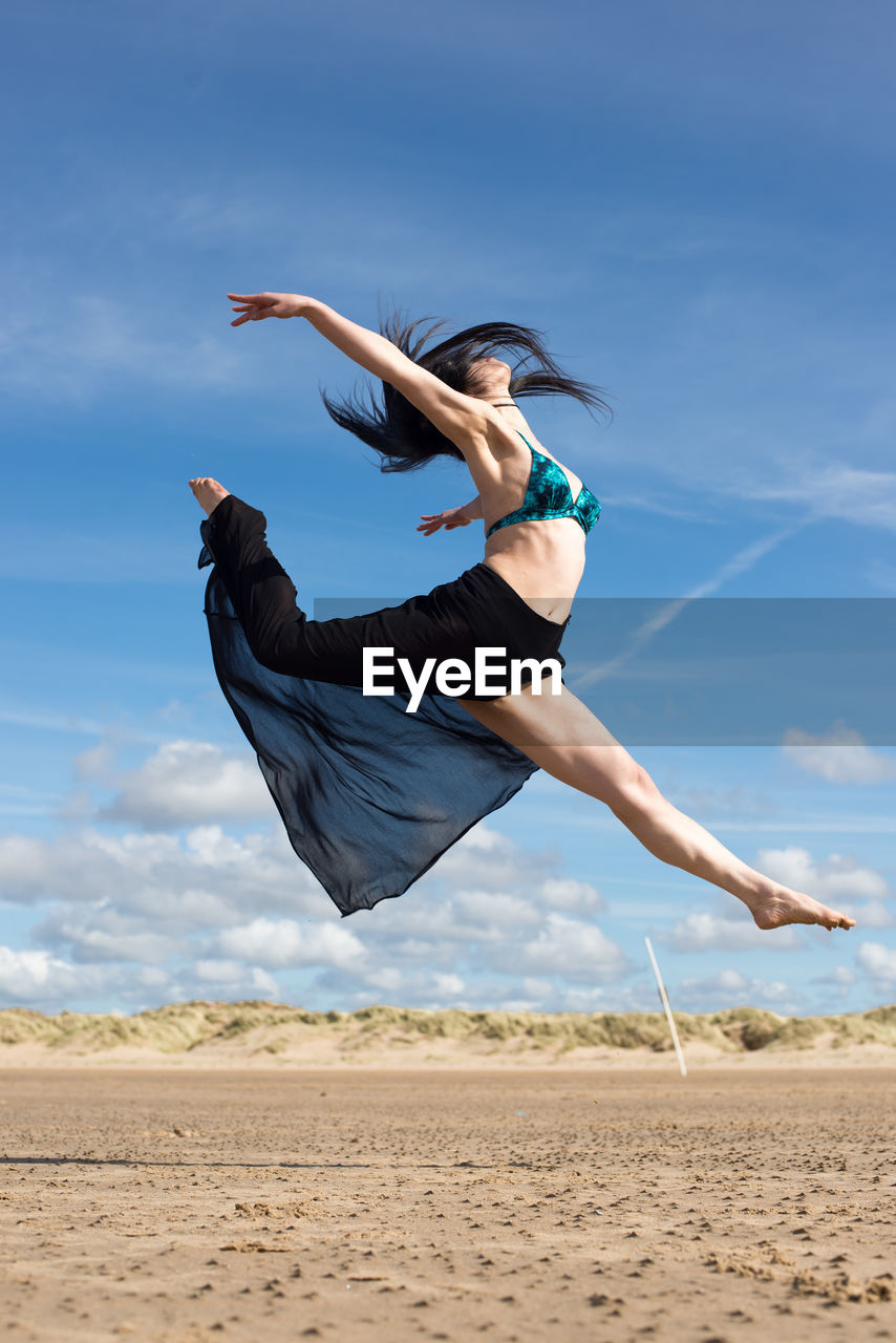 YOUNG WOMAN JUMPING ON BEACH