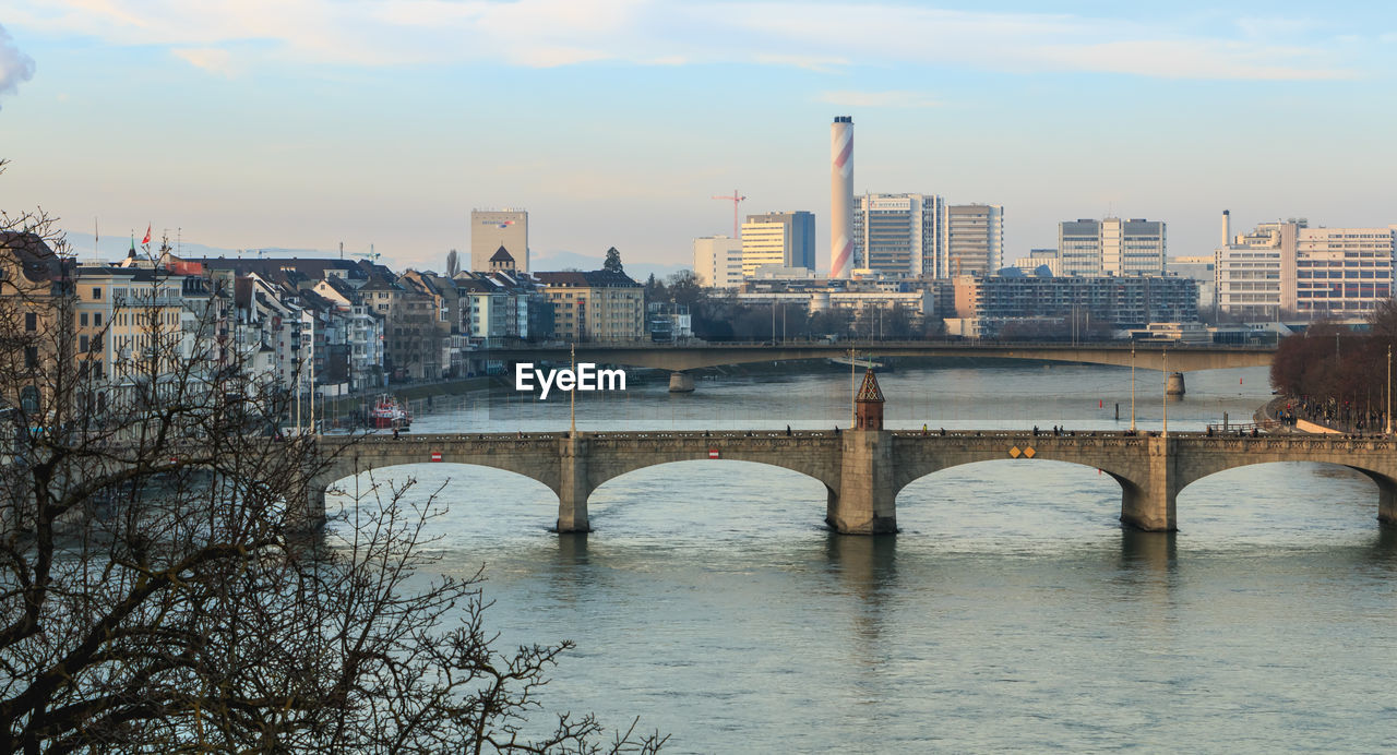 Bridge over river by buildings against sky in city