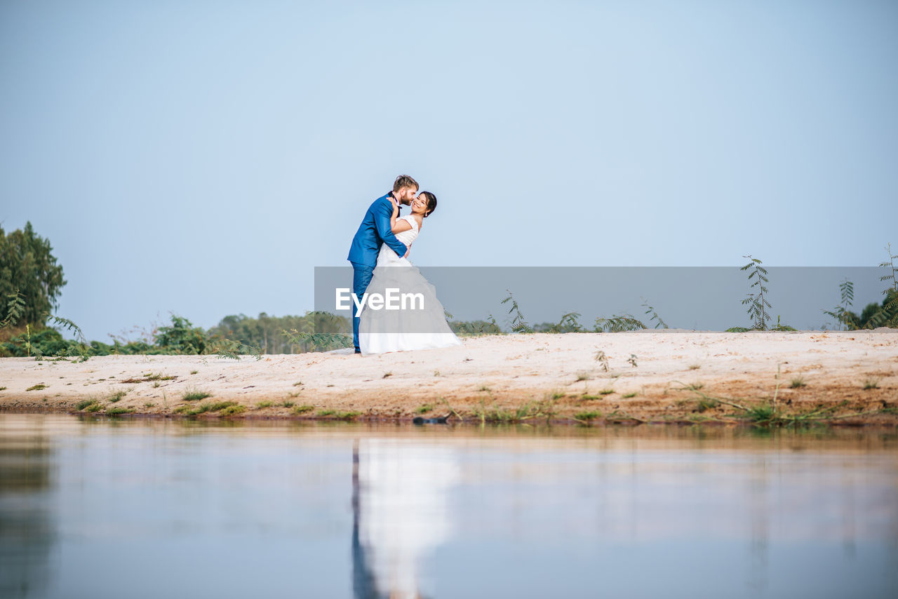 Couple embracing by lake against trees and sky