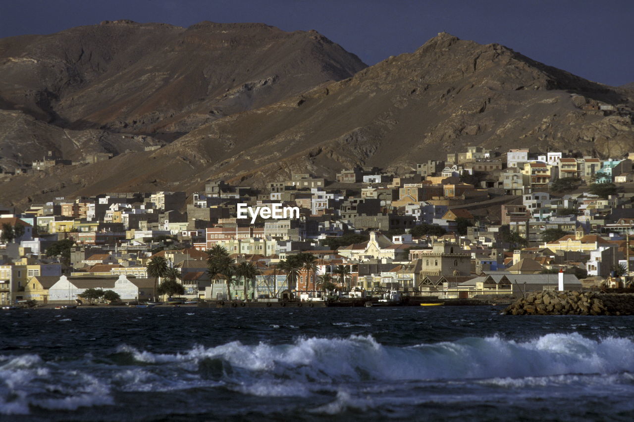 Sea in front of buildings on mountains