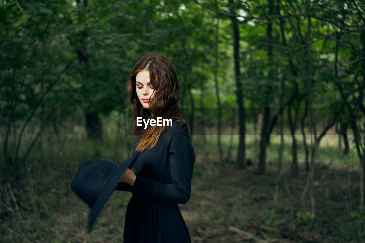 young woman standing against trees in forest