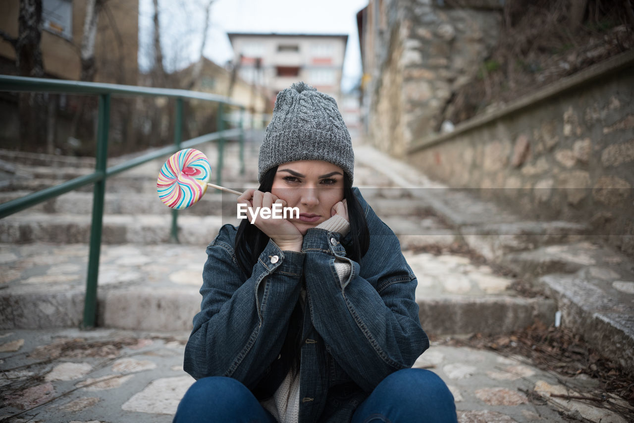 Portrait of young woman having lollipop while sitting on steps