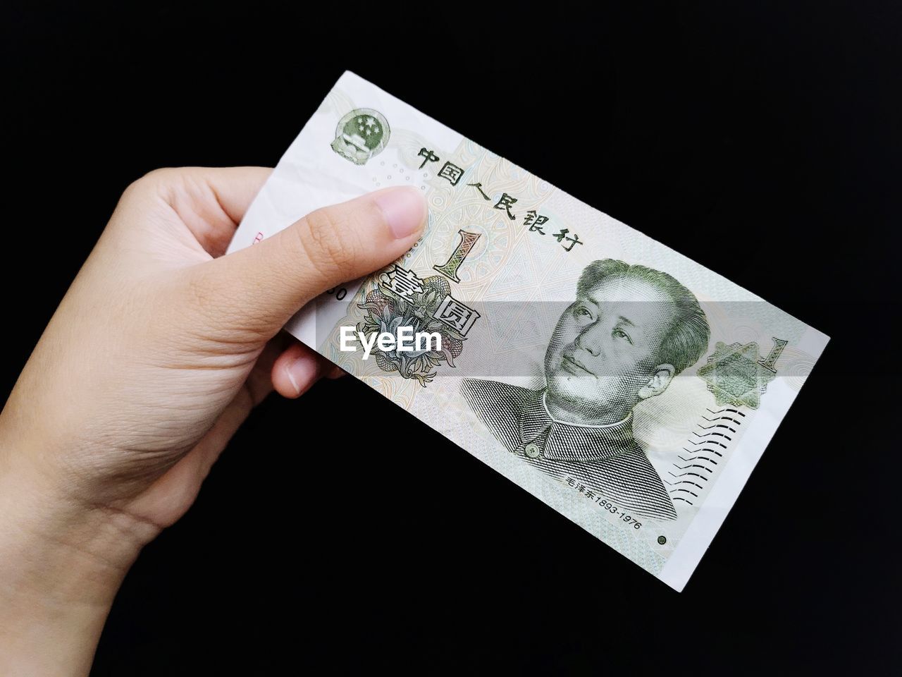 Cropped hand of person holding paper currency against black background