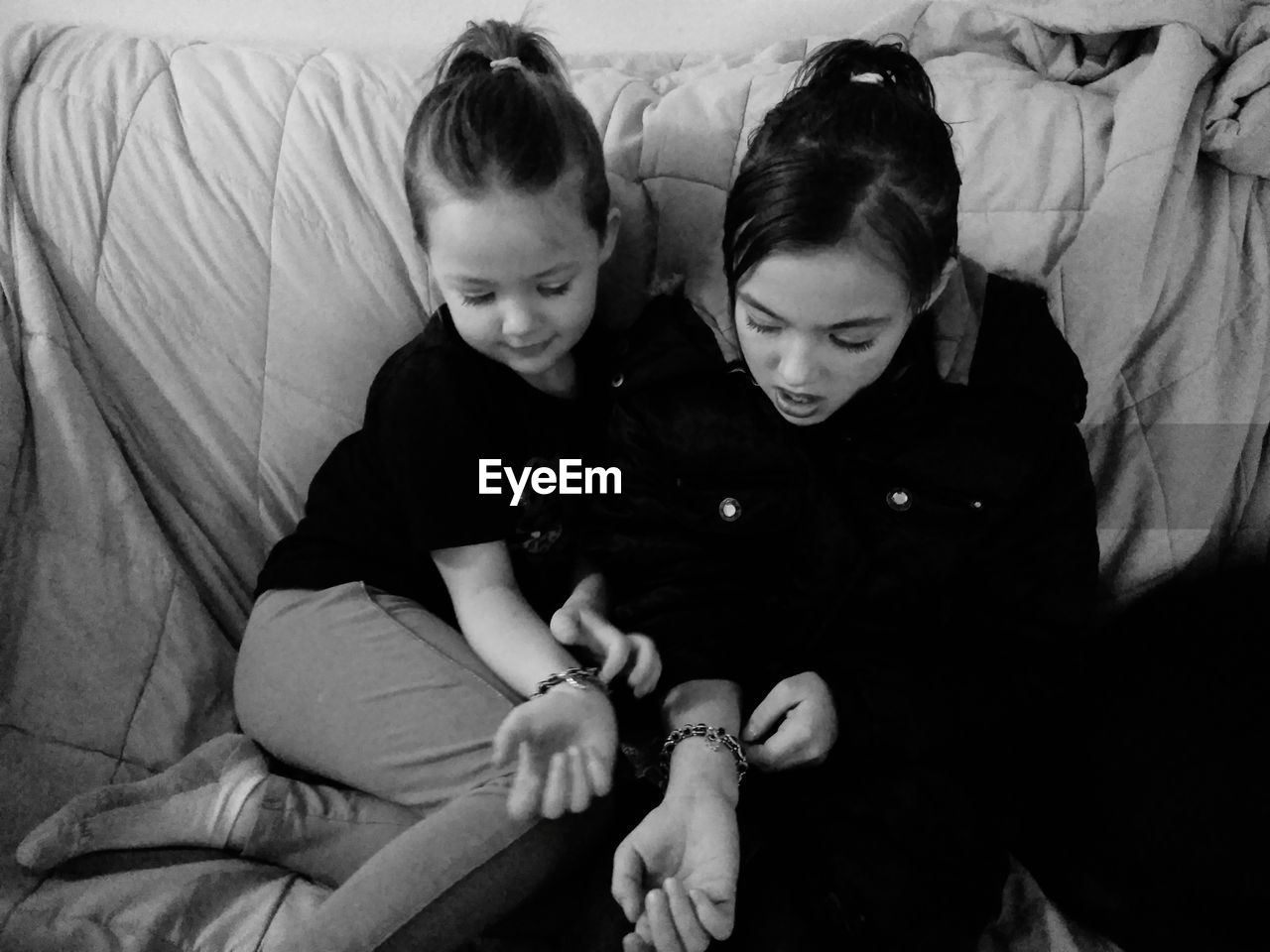 High angle view of sisters wearing bracelets while sitting on sofa at home