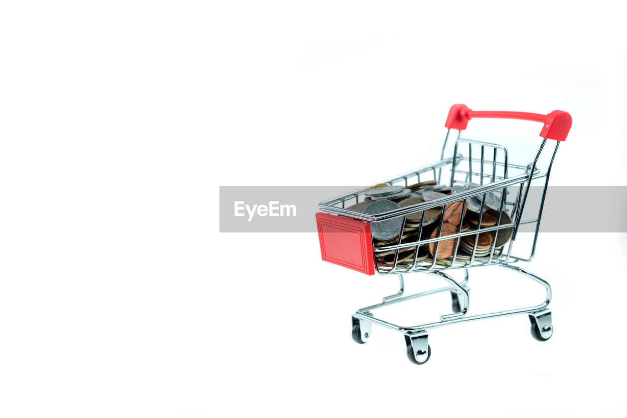 Close-up of coins and shopping cart over white background