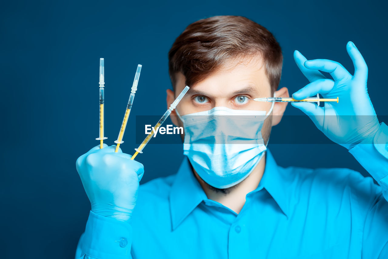 Portrait of doctor wearing mask holding syringes