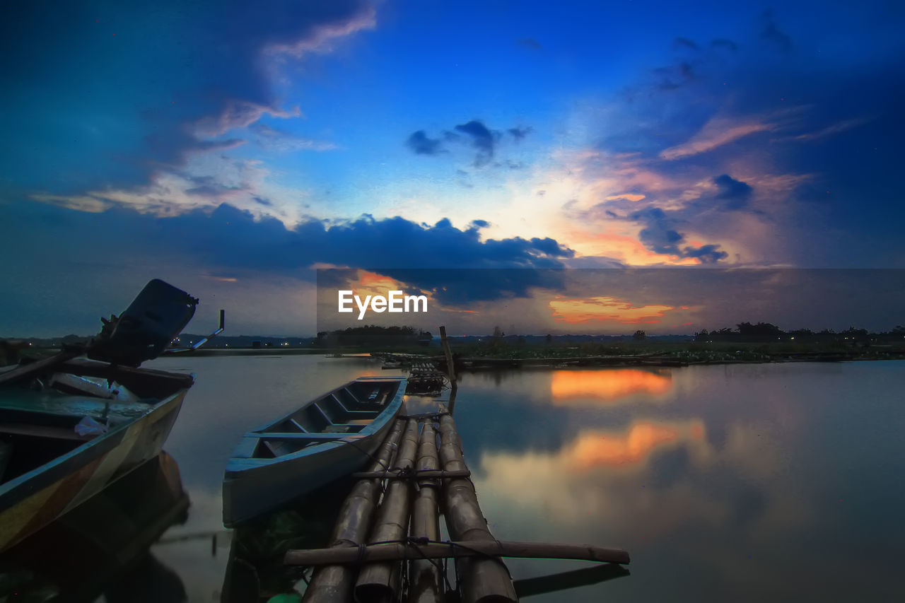 Sailboats moored in lake against sky during sunset