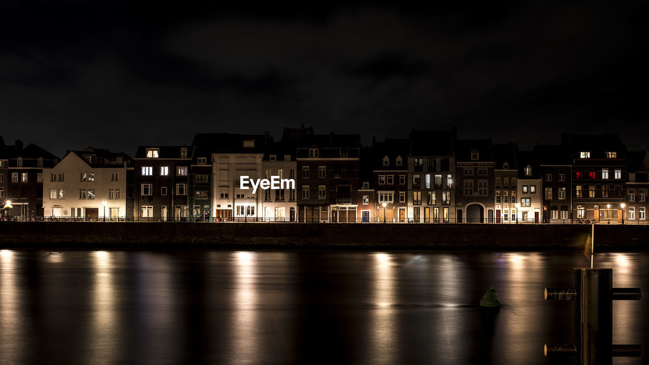 Illuminated buildings by river against sky at night