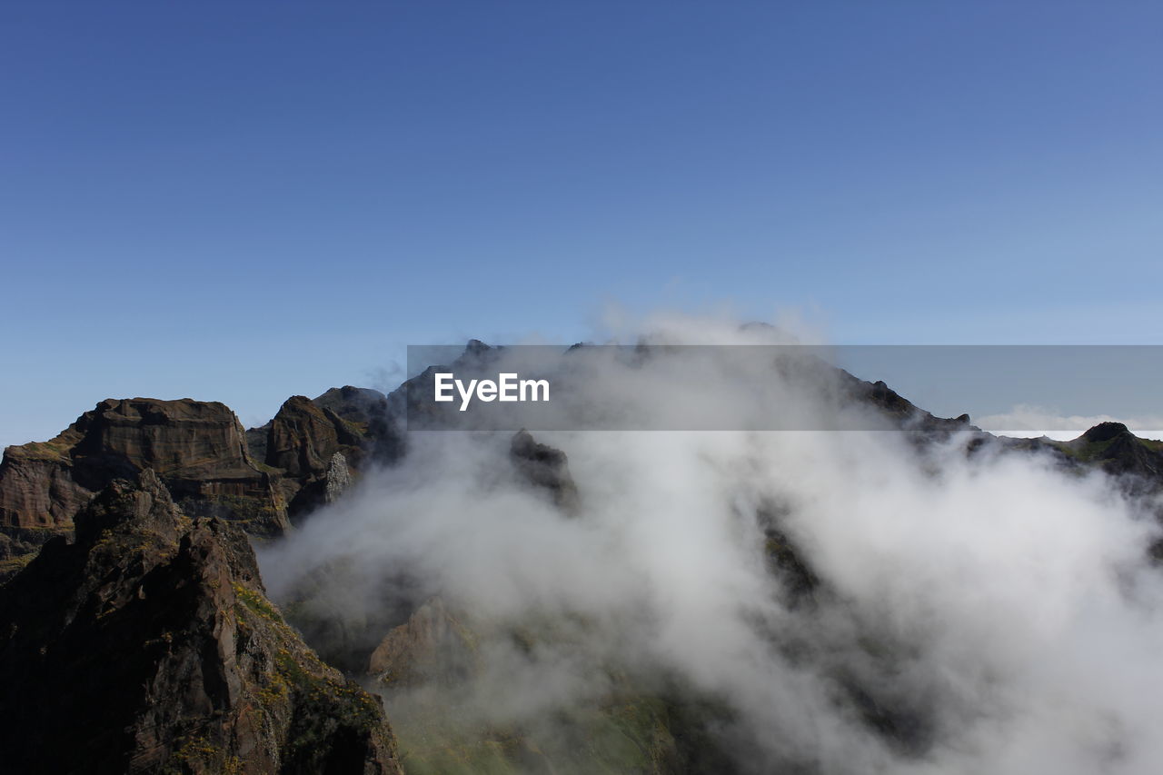 Smoke emitting from volcanic mountain against clear blue sky