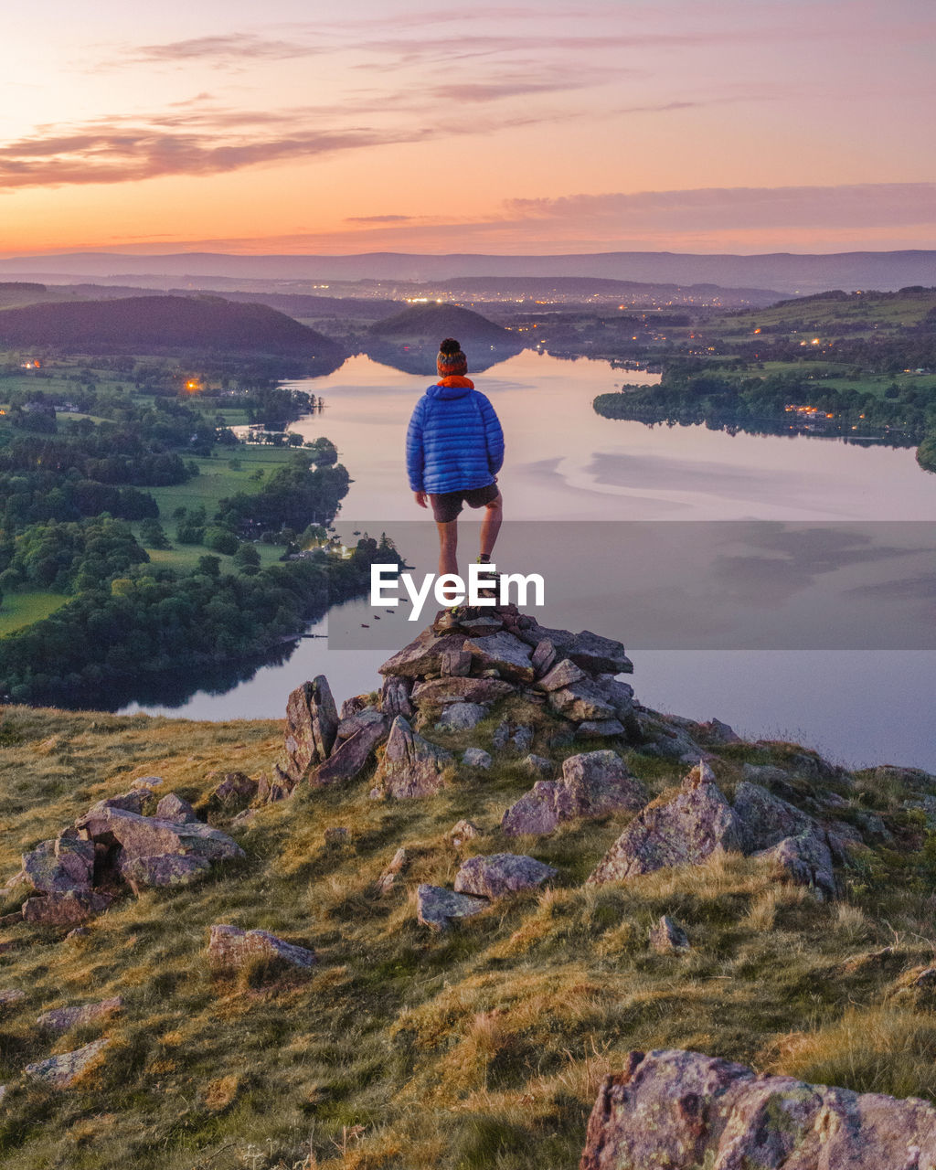 Hiker shot from behind stood on mountain looking over a lake at sunset